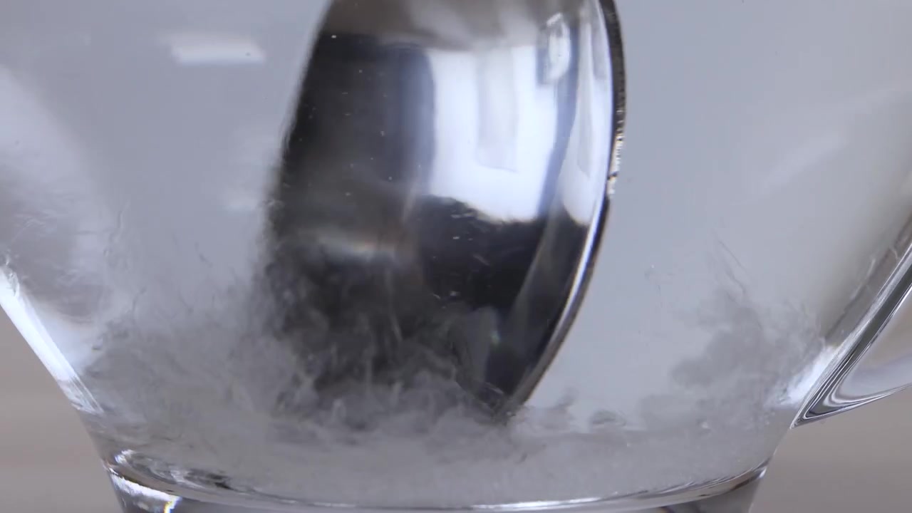 Primo piano di zucchero bianco che si scioglie in acqua calda mentre viene mescolato in una tazza di vetro