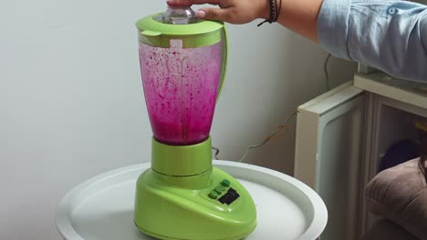 mujer con la mano en la máquina de mezclador para la preparación de frutas mezcladas