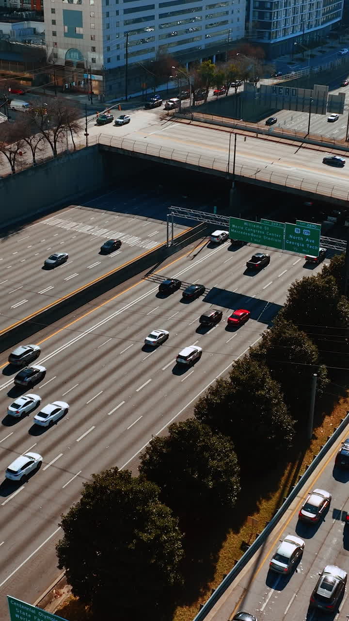 Numerous cars run by the multilane road in downtown of Atlanta on daytime. Sunny panorama of the city from top. Vertical video