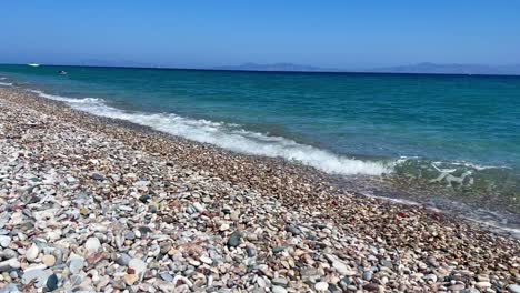 Cobble-Beach-in-Rhodos,-Greece-with-Marmaris-in-the-far-end,-blue-crystal-clear-water,-travel-destination-and-establishing-shot-filmed-in-4K