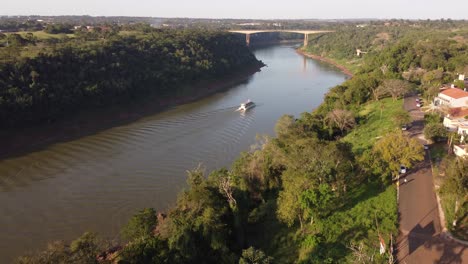 tourist boat sailing along iguazu river at border between argentina and brazil at sunset with tancredo neves bridge in background