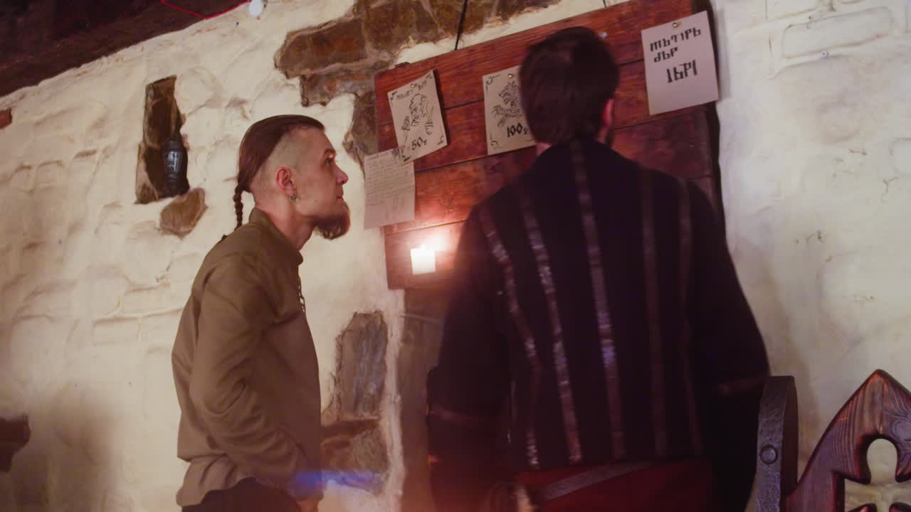 los amigos leen mensajes en el tablón de anuncios en la taberna. los hombres pobres estudian anuncios en lenguaje imaginario para convertirse en héroes en el pub. los campesinos borrachos en el bar.