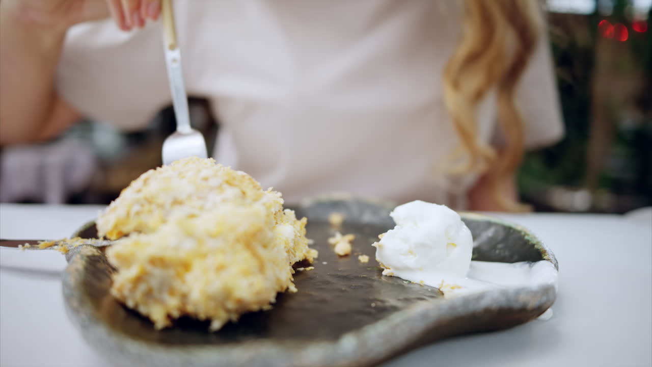 Close view of a woman eating a cake with ice cream with a fork in a cafe