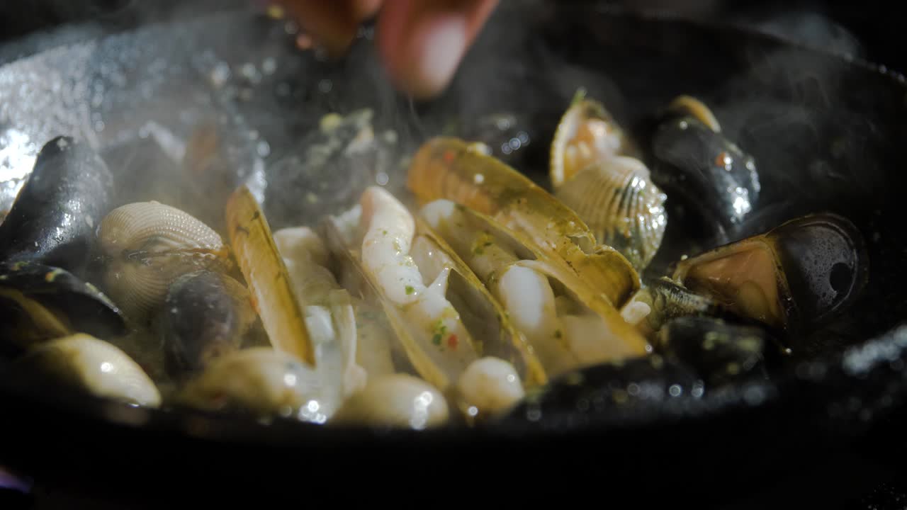 mejillones y mariscos cocinados en una sartén, siendo arrojados alrededor