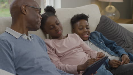 grandfather reading a story on an electronic tablet to grandchildren