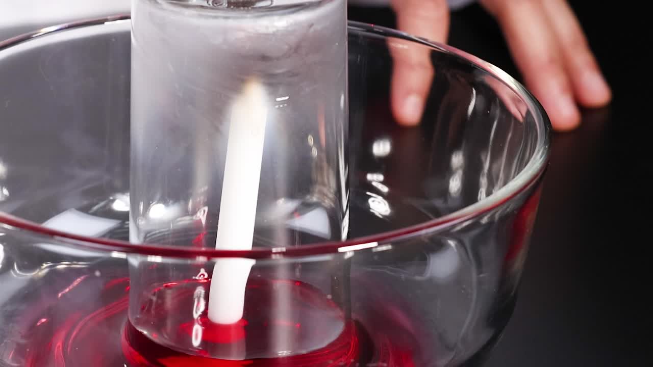 Observe the candle flame affecting water levels in a glass container.