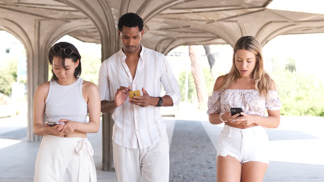 Multiracial friends using smartphones in colonnade structure