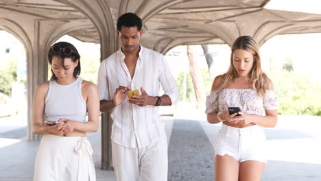 multiracial friends using smartphones in colonnade structure