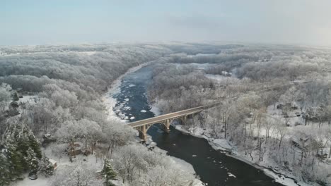 Vista-De-ángulo-Alto-Del-Majestuoso-Puente-Sobre-El-Río-Congelado-Y-El-Bosque-Helado