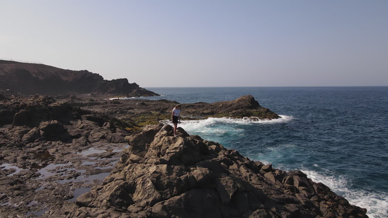 Aerial view: Young woman enjoying the scenic Gran Canaria coastline from volcanic rocks
