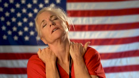 medium tight portrait of nurse looking overwhelmed and stressed, hands on her neck with american flag behind her