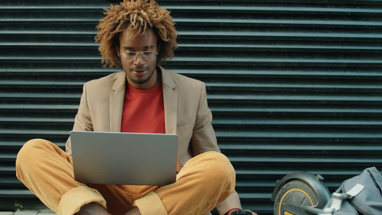 African American Man Working on Laptop and Drinking To Go Coffee on Street