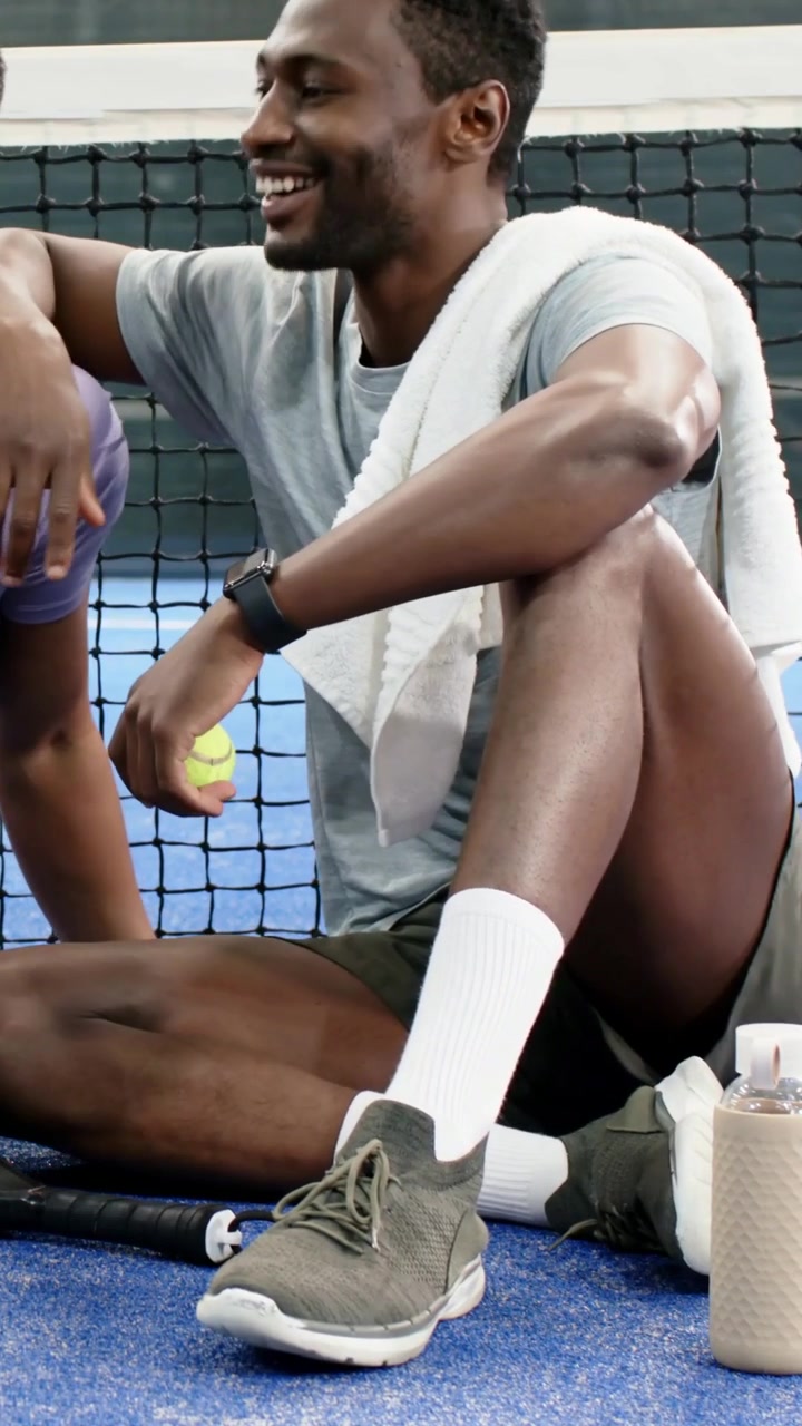 Vertical video: Rolling tennis ball after practice, man in gray with towel helping pal on court