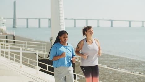 long shot of happy women jogging along embankment