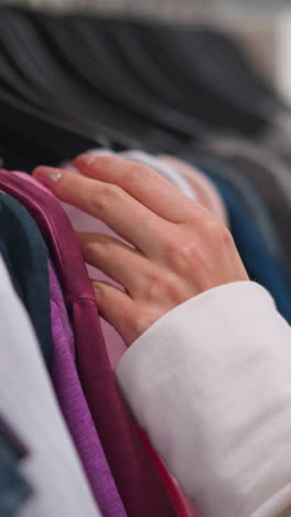 primer plano de la mano femenina revisando cuidadosamente el colorido estante de ropa, centrándose en texturas suaves y colores de telas vibrantes en la tienda minorista, mostrando una experiencia de compra reflexiva y opciones de moda