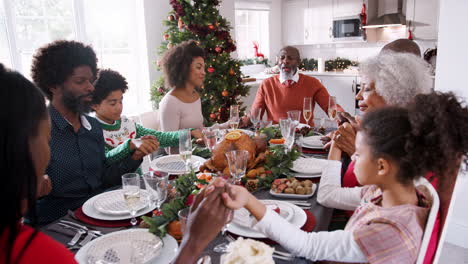Multi-generation-mixed-race-family-sitting-at-Christmas-Day-table-holding-hands-and-saying-grace,-selective-focus,-elevated-view