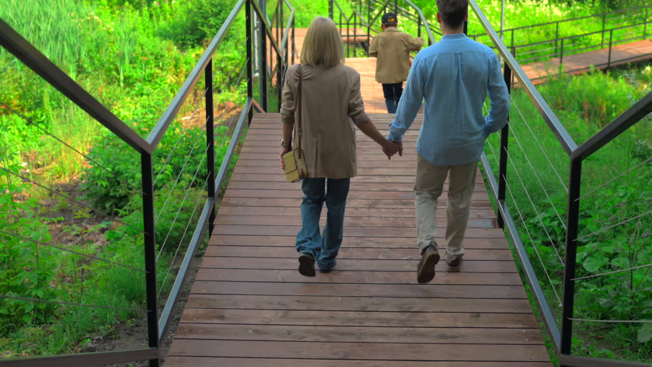 Couple Holding Hands Walking on Wooden Bridge