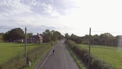 a biker rides into a village in the uk.  drone shot where the camera gradually gets higher and reveals the rural landscape.