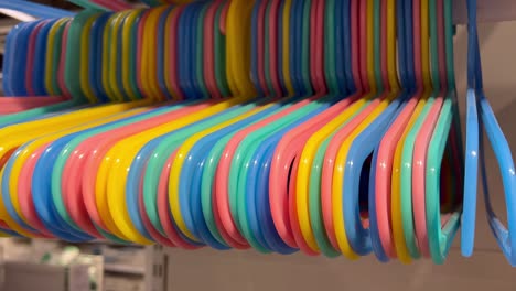 blue, yellow, orange, pink, and green hangers of different colors are suspended from the white pipe