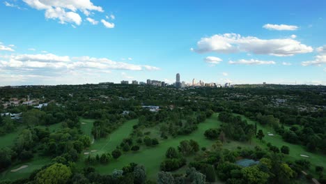 green golf course with skyline of sandton in johannesburg during day, aerial