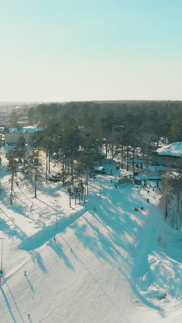 people ski on modern snowy mountain resort tracks at dense forest on cold winter day aerial view