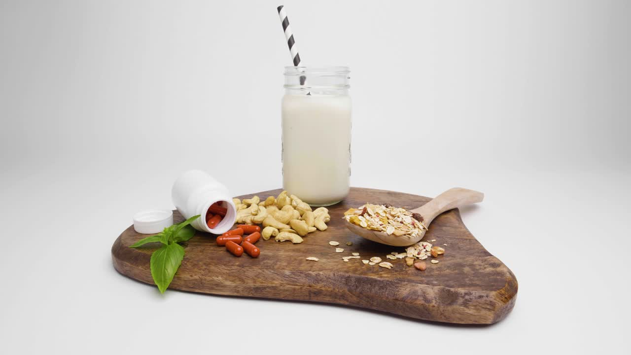 toma de pan de una tabla de cortar con albahaca, pastillas rojas saludables con envoltura de tableta blanca y nueces de anacardo con cereales contra fondo blanco