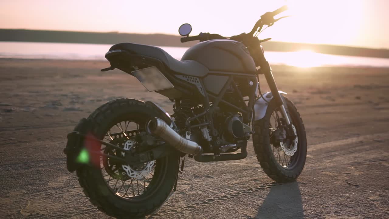 una motocicleta estacionada en el suelo cerca del agua en el atardecer, fondo borroso
