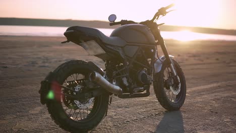 una motocicleta estacionada en el suelo cerca del agua en el atardecer, fondo borroso