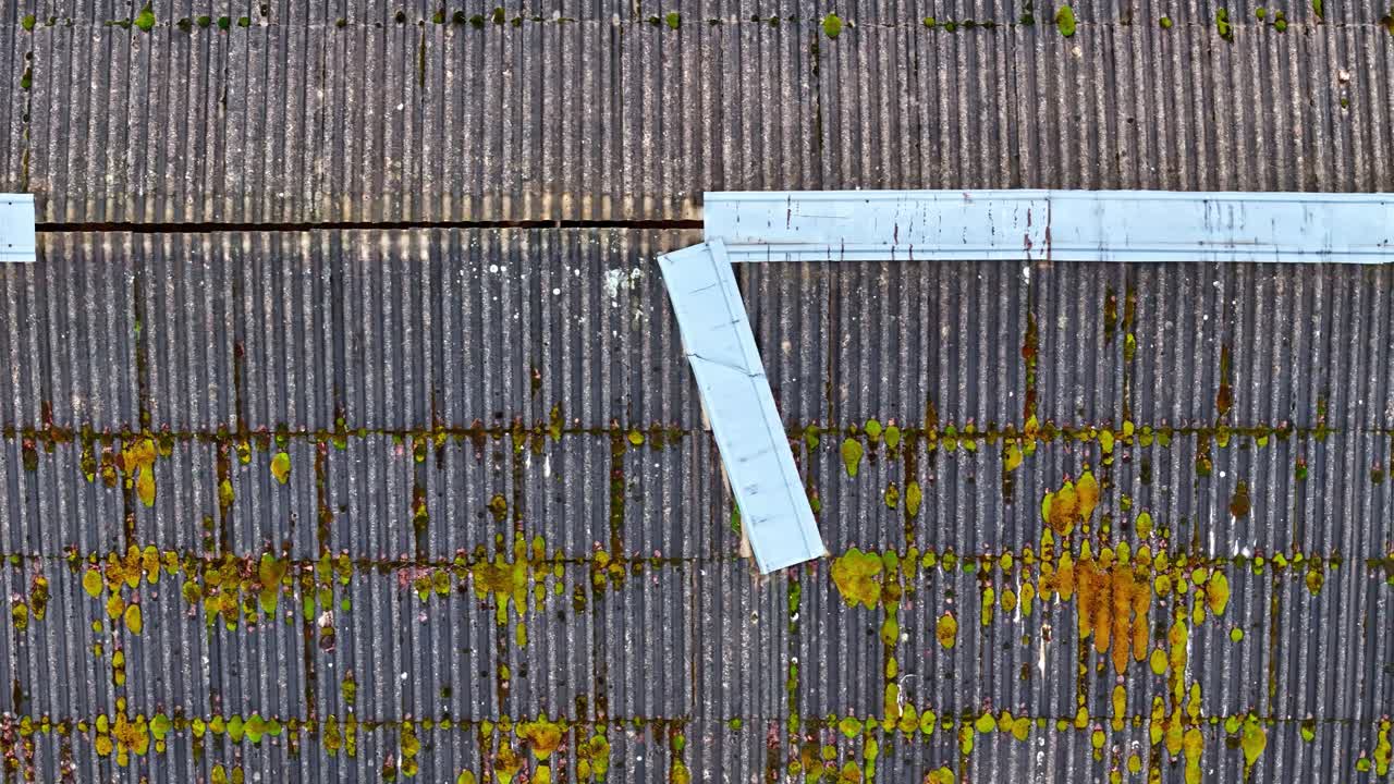 Vista aerea dall'alto di un tetto di tegole con linee di bordo bianche e chiazze di muschio, che mostra possibilmente parte di un marciapiede o di una strada, catturata da drone.