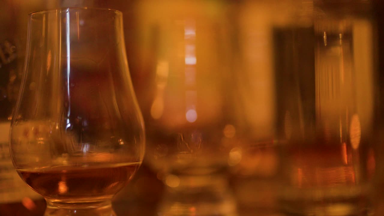 Amber whisky glass on bar, shallow focus, warm evening lighting, subtle camera movement, cozy atmosphere
