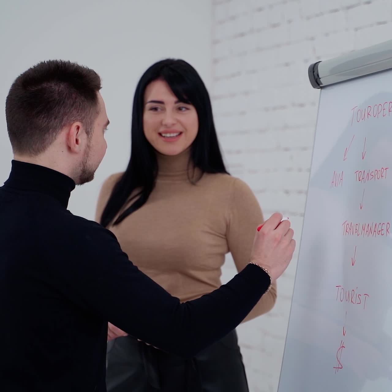Business workers talk about their company. Man is writing on a board while pretty woman talking to him and smiles.Young couple working in office.
