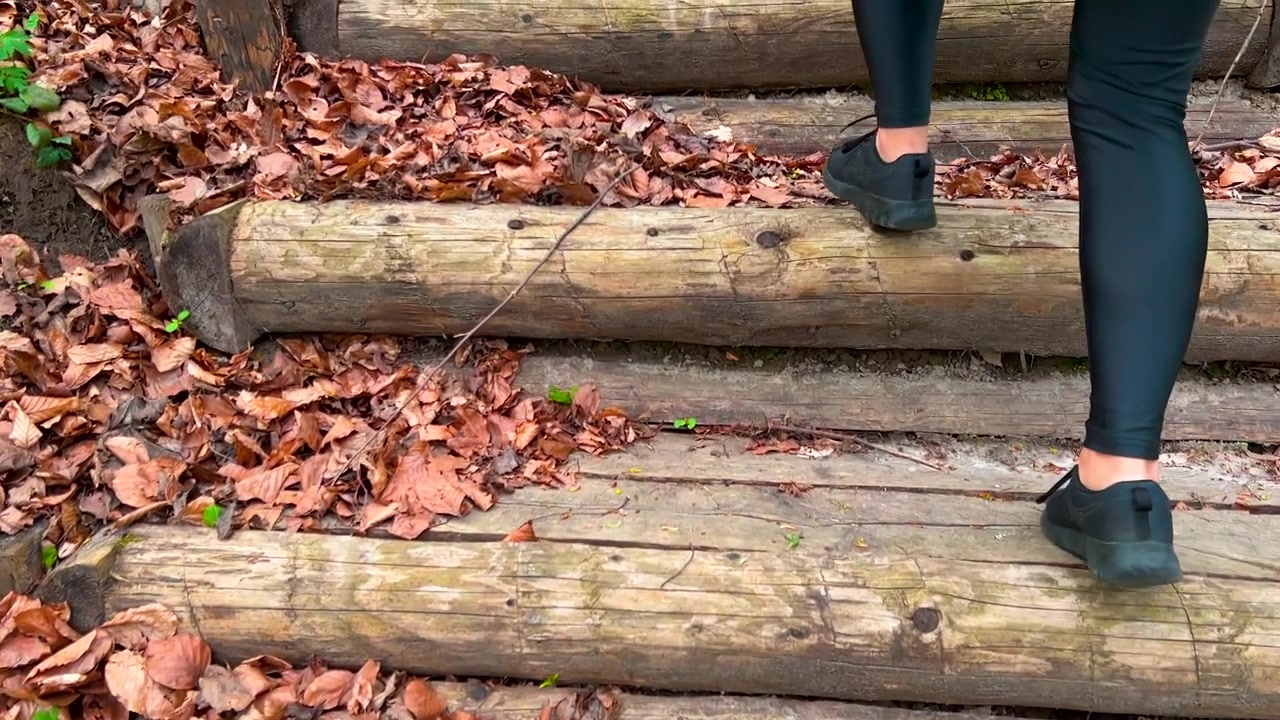 Legs close-up of woman in sports shoes walking up wooden stairs made of tree logs in Spring Forest trail - following rear view