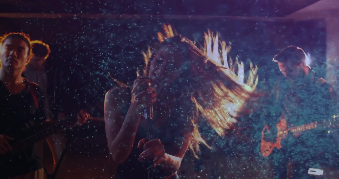 La cantante solista afferra un microfono cablato, facendo headbanging dopo il segnale del batterista, creando una foschia di luce di contorno musicale.