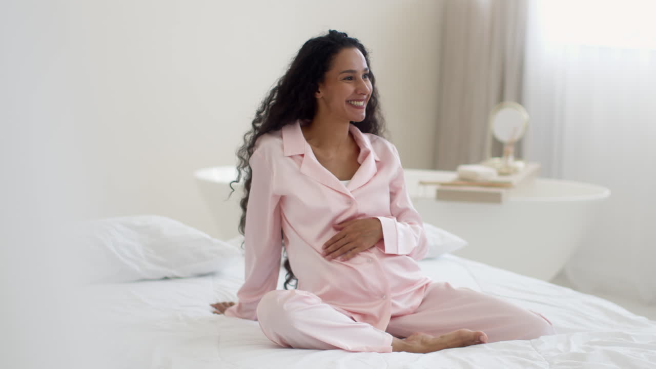 Pregnant woman in pink pajamas sitting on a bed
