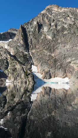 Vertikal-4k,-Spiegelung-Auf-Gletschersee,-Hügeln,-Klippen-Und-Himmel-An-Einem-Sonnigen-Tag-In-Den-Bergen