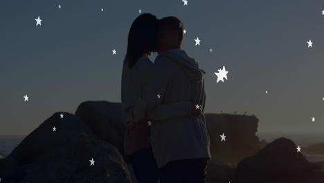 couple embracing and kissing on rocky shore at dusk, boosting social media ads with star graphics