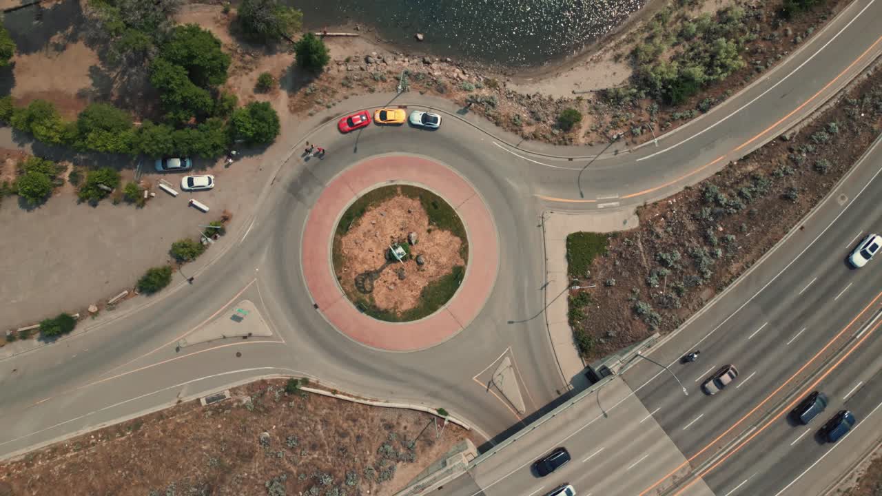 Bird's eye Aerial view of three super cars parked in a roundabout on the edge of Okanagan Lake Kelowna BC with camera ascending slowly rotating