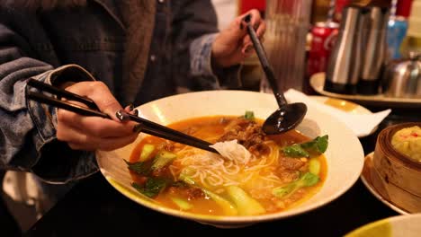 person enjoying chinese noodle soup with chopsticks