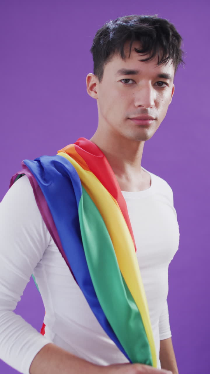 Vertical video of portrait of happy biracial man holding lgbt flag