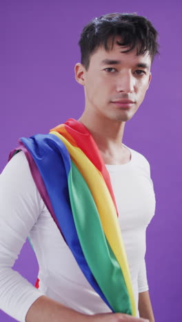 video vertical del retrato de un hombre biracial feliz sosteniendo una bandera lgbt