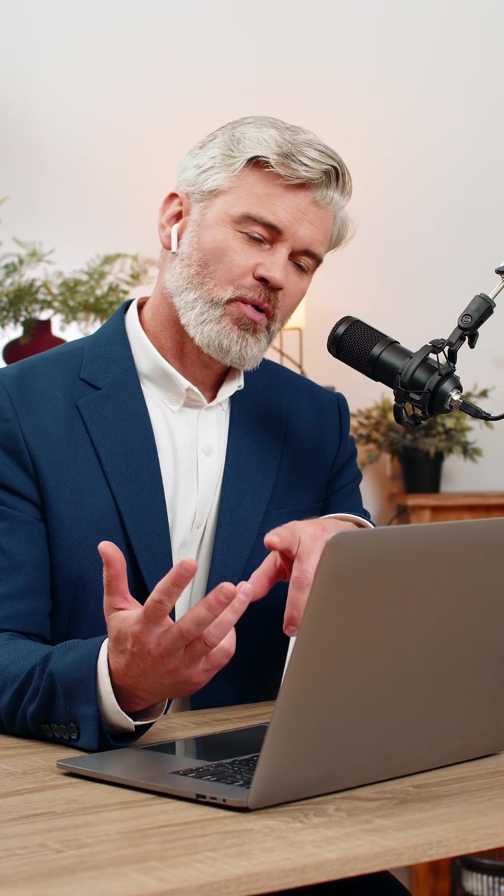 Midaldrende forretningsmand optager podcast på studiemikrofon, gestikulerer aktivt og deler live-idéer