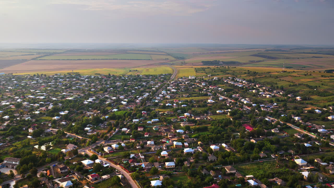 Aerial drone view showing a Moldovan village surrounded by vast farmlands and open fields under a hazy autumn sky