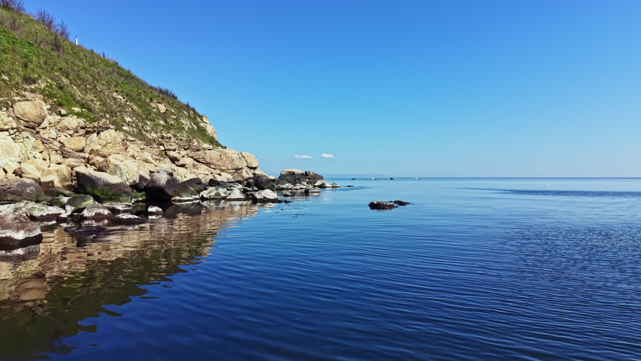 Ruhiger Blick auf ruhiges Wasser und felsige Küste entlang der Küstenlinie an einem klaren und sonnigen Tag in Strandnähe.