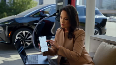 woman engaged with phone and laptop while electric vehicle charges
