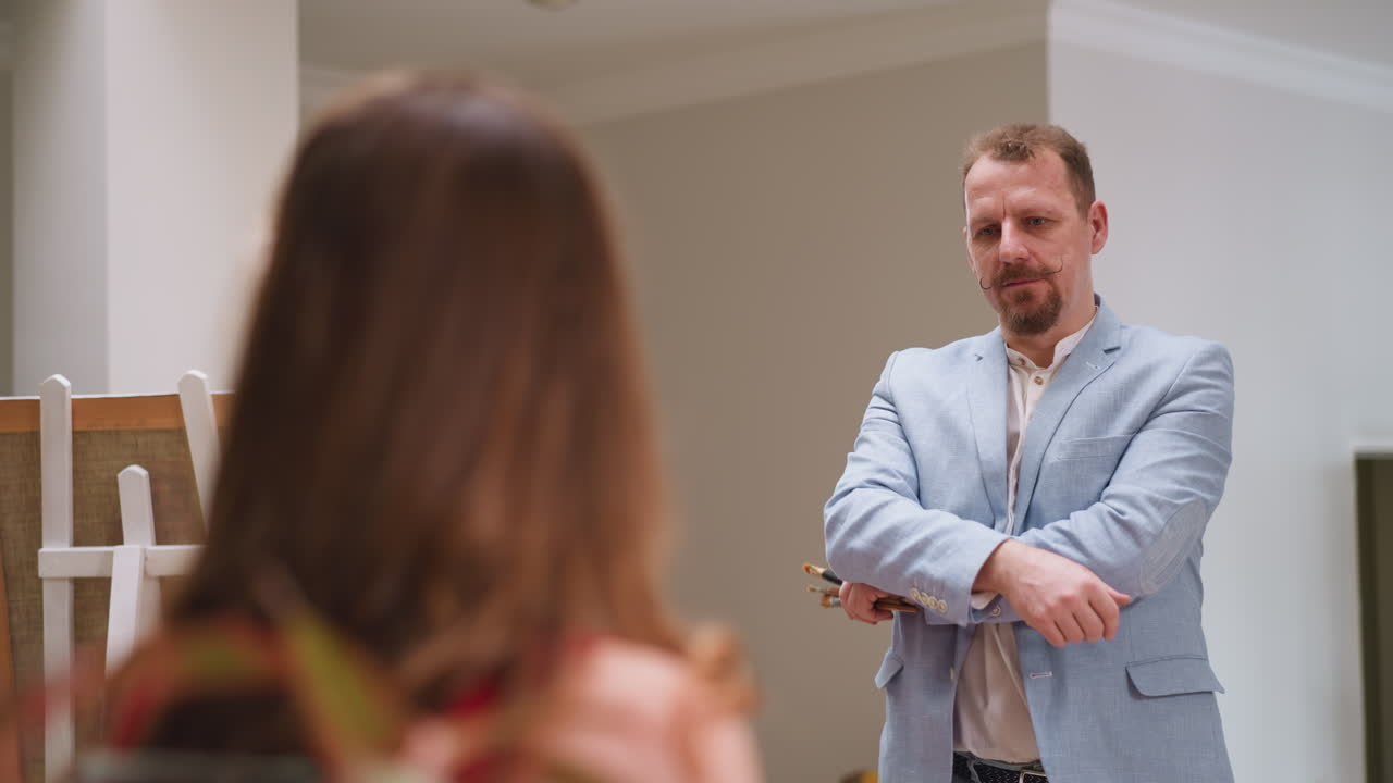 el artista mira a la modelo buscando una postura adecuada en el estudio. hombre enfocado con barba y pinceles grupo mira a la mujer morena en la tienda de arte. pintor creativo en el trabajo