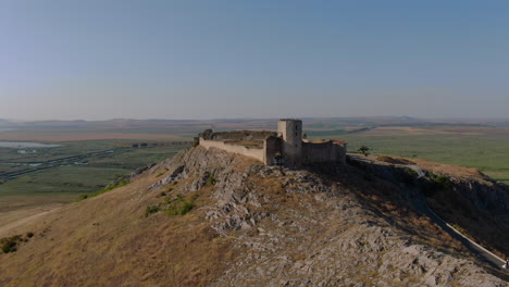 Dolly-zoom-shot-of-Enisala,-medieval-fortress-on-top-of-a-hill-surrounded-by-lakes-and-plains-on-a-clear-sunny-day