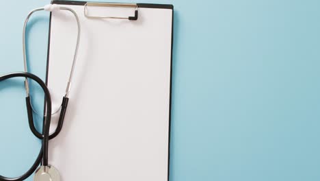 video of stethoscope with blank white paper on clipboard, on blue background with copy space