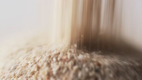 Video-of-close-up-of-sand-grains-pouring-into-heap-and-copy-space-on-white-background