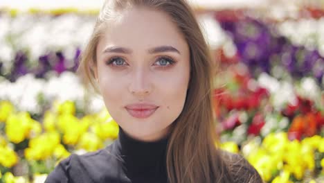 beautiful female with blue eyes and makeup posing on blurred background of colorful flowers