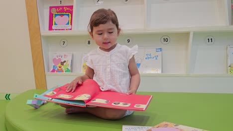 3-year-old little girl reading and turning page of children's book while sitting on the floor